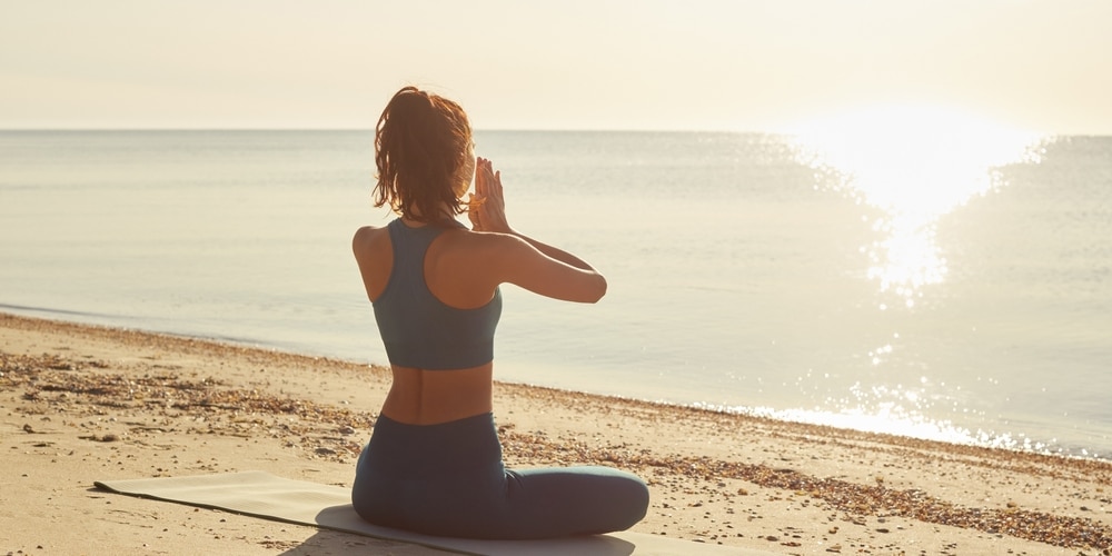 Fitness woman doing yoga outdoors practices meditation on a beach at sunrise